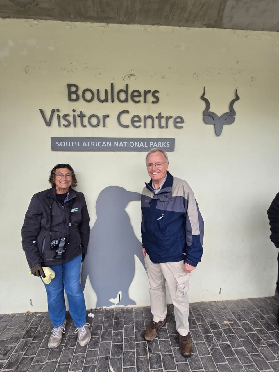 Couple at the Boulders Visitor Centre with the penguin silhouette on the wall