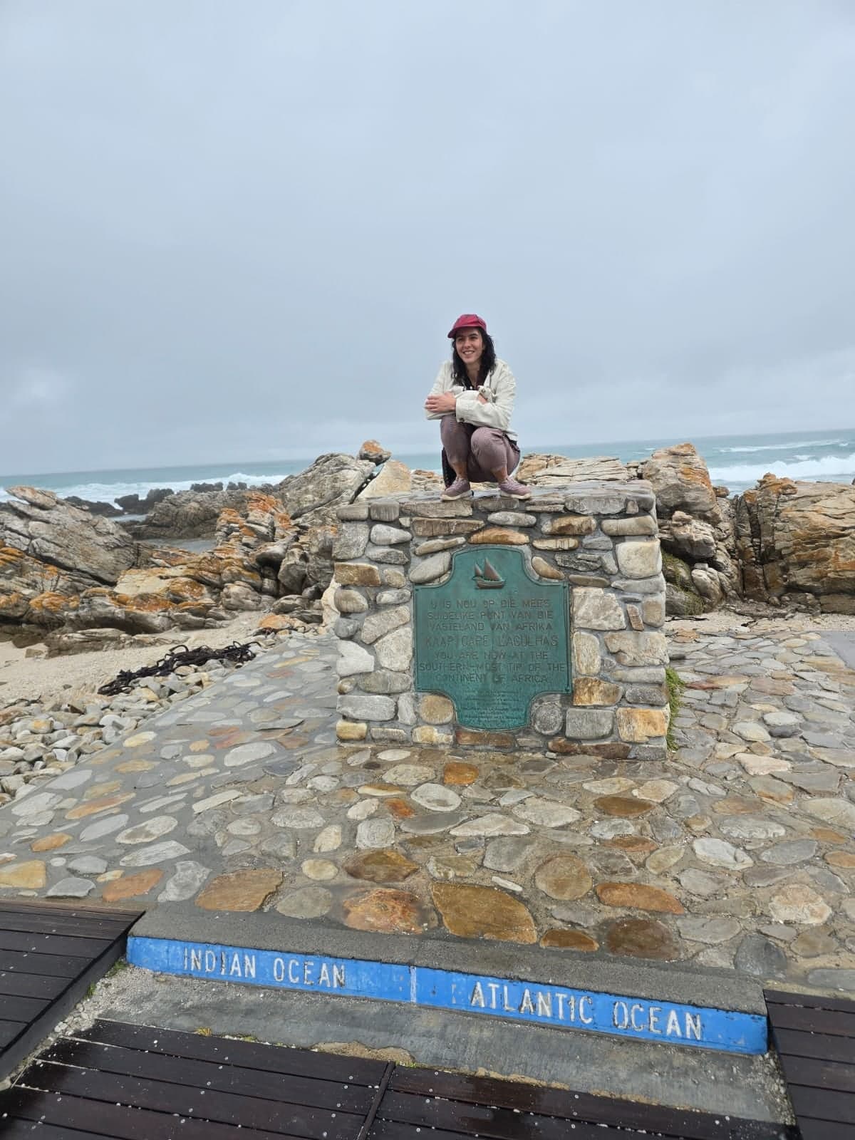Guest sitting on the marker where the Indian and Atlantic oceans meet at Cape Agulhas