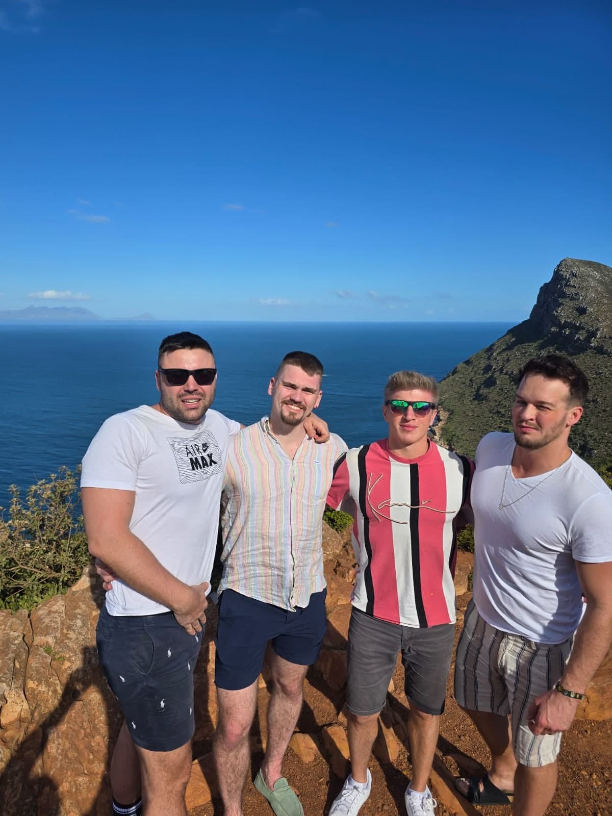 Four friends on a clifftop at Cape Point with the ocean behind them